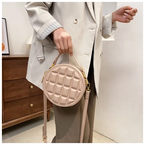 Close-up of quilted beige leather round crossbody bag with gold hardware and top handle