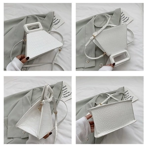 Detail view of white crocodile pattern trapezoid handbag with gold hardware and shoulder strap
