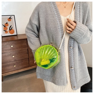Détail du sac coquille en acrylique vert avec bandoulière perle sur tenue