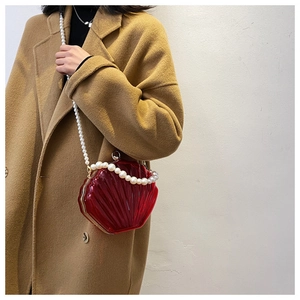 Sac coquille rouge translucide avec bandoulière en perles porté sur un manteau