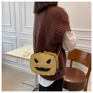 Detail of sequined pumpkin bag with gold chain and bat charm worn on a brown sweater