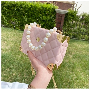Close-up of pink quilted box bag with pearl handle and golden floral ornament