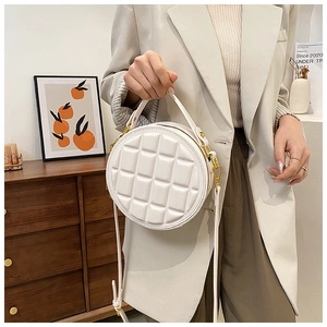 Detail of white round quilted crossbody bag with golden zipper held by a model