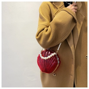 Détail du sac coquille en acrylique rouge avec bandoulière perles sur un manteau beige