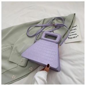 Detail of purple crocodile-patterned trapezoid handbag on green shirt background