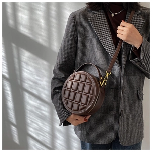 Macro shot of dark brown round bag with chocolate cube textured pattern and gold hardware