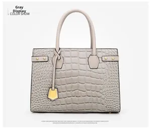 Detail of grey crocodile embossed handbag featuring golden lock charm and round handles