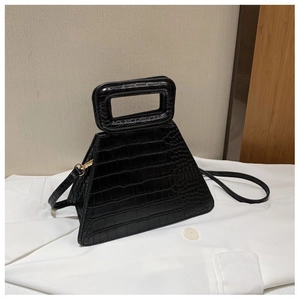 Close-up of black crocodile embossed trapezoid handbag with hollow hard handle and gold hardware