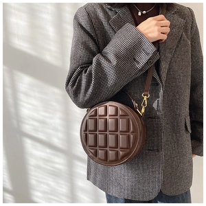 Close-up of circular brown crossbody bag featuring embossed quilted texture and gold hardware
