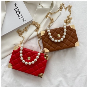 Close-up of quilted crossbody box bag featuring pearl handles and gold corner protectors