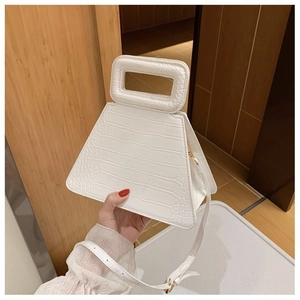 Detail view of the white crocodile pattern on a trapezoid handbag with a metal buckle strap
