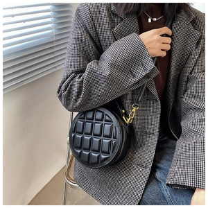 Detail of black round crossbody bag featuring chocolate quilt pattern and gold buckles