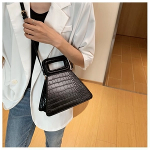 Detail of black crocodile texture handbag featuring unique triangular shape and long strap