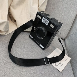 Schwarze Umhängetasche im Retro-Kamera-Design mit breitem Gurt auf grauem Sofa