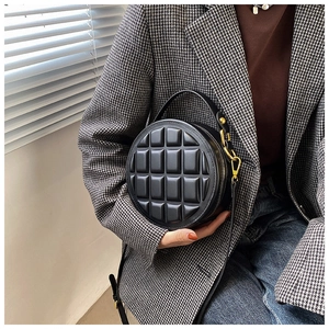 Close-up of black round quilted bag with embossed grid pattern and metal zipper detail