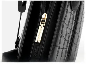 Detail of polished gold zipper puller and embossed crocodile texture on black handbag