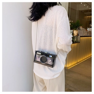 Detail of camera-shaped crossbody bag with silver chain strap worn on a stylish model