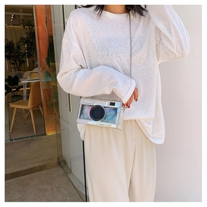 Detail of silver camera-shaped crossbody bag with feathers and metal chain strap