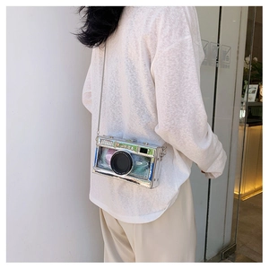 Modern transparent camera-shaped crossbody bag with silver chain worn by a model