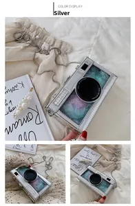 Detail of silver camera-shaped crossbody bag with transparent window and colorful feathers