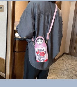 Detail showing pink Matryoshka doll crossbody bag with vibrant floral print on model back