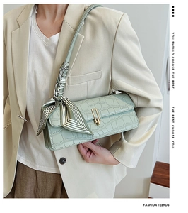 Detail of light green crocodile pattern handbag with gold clasp and decorative silk scarf