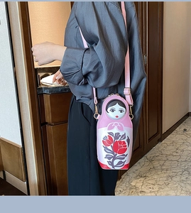 Pink Russian nesting doll shaped PU leather crossbody bag worn by a female model