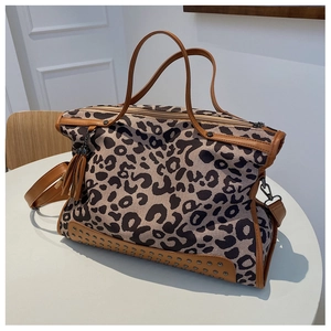 Borsa tote leopardata con finiture in pelle marrone e rivetti su un tavolo bianco