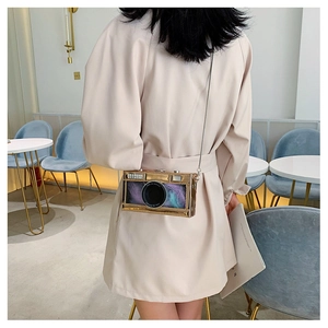 Detail of gold camera-shaped crossbody bag with feather accents and metal chain strap