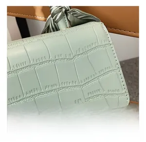 Detail showing green crocodile texture handbag with striped silk scarf wrapped on handle