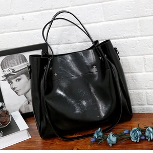 Detalle del bolso tote negro brillante con anillas metálicas y cuero sintético texturizado