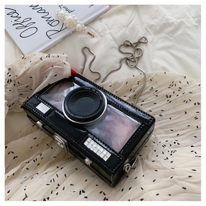 Detail of a camera-shaped box bag with glitter lens and metal chain on fabric