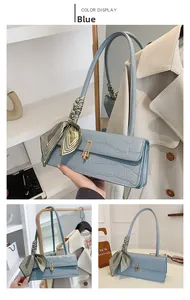 Detail of light blue crocodile embossed handbag with golden buckle and silk scarf strap decor