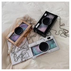 Close-up of camera-shaped chain bags in gold, silver, and black with colorful feathers