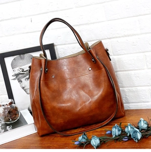 Detalle del bolso tote vintage marrón oscuro con asas dobles y remaches sobre madera