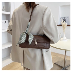Detail of dark brown faux crocodile baguette bag with stylish green striped scarf wrap