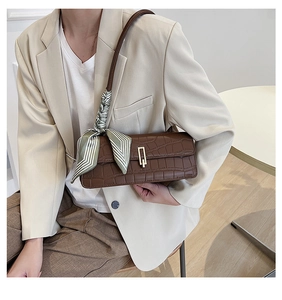Close-up of brown crocodile texture bag with gold clasp and decorative silk scarf detail