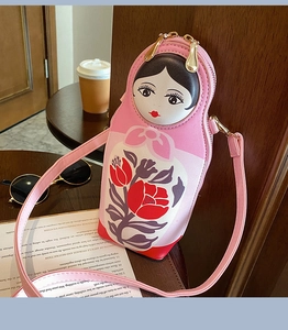 Pink Matryoshka doll crossbody bag with cartoon face and floral details on a wooden table