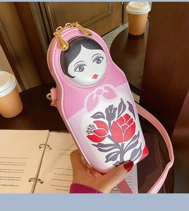 Detail of pink Russian nesting doll crossbody bag with floral patterns on a wooden desk