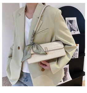 Detail of stone-textured cream crossbody bag with gold buckle and green silk scarf decor