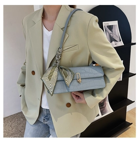Detail of light blue croc-embossed handbag with gold clasp and striped silk scarf