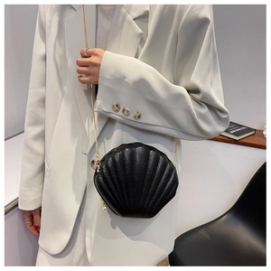 Detail of black shell-shaped crossbody bag with pearl pendant and golden chain strap