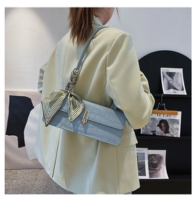 Detail of light blue crocodile pattern bag with decorative striped silk scarf and gold buckle