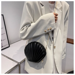 Detail of shell-shaped crossbody bag with gold chain and pearl zipper pendant