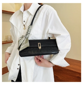 Detail of black faux crocodile leather shoulder bag with decorative silk scarf and gold clasp