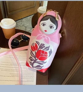 Detailed close-up of pink Russian doll PU crossbody bag with floral print on wooden table