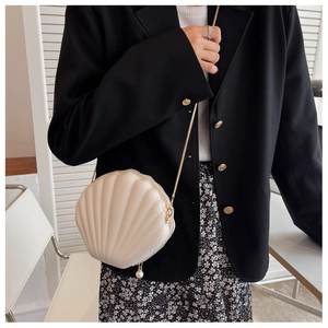 Detail of off-white shell-shaped crossbody bag with pearl charm and gold chain strap