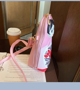 Pink Matryoshka doll shaped crossbody bag with floral patterns on a wooden desk