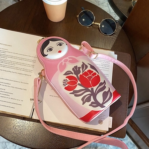 Pink Matryoshka PU leather crossbody bag with floral patterns on a dark wooden table