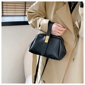 Detail of black pebbled leather shell bag with gold clasp worn with a beige trench coat